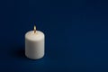 One whiteÃÂ burningÃÂ candle onÃÂ dark blue backgroundÃÂ withÃÂ copyÃÂ space forÃÂ text Royalty Free Stock Photo